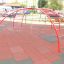 Rosso Cross Climber steel structure in un parco giochi con tappeti di sicurezza.