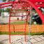 Rosso Cross Climber steel structure in un parco giochi con sabbia e una corda appesa.