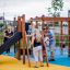 Struttura da parco giochi in legno Climbing Kiosk Nature con scivolo e rete da arrampicata, bambini che giocano