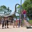Bambini che giocano sulle attrezzature da gioco Silver Cableway con una statua di dinosauro sullo sfondo