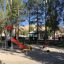 Yacht Swing rocking in un vivace parco giochi con scivolo colorato e alberi sullo sfondo.