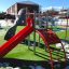 Parco giochi Whale - AZTEC steel structure con scivolo rosso e pareti da arrampicata su un prato verde.