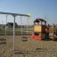 Baby Double Swing in un parco giochi con una casetta e una struttura da arrampicata.