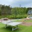 Attrezzature da parco giochi tra cui Triple Somersault e un tavolo da ping pong su erba artificiale.