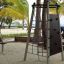 Struttura da arrampicata in acciaio su una spiaggia sabbiosa con palme sullo sfondo.
