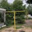 Youth Double Swing giallo in un parco giochi con vegetazione sullo sfondo.