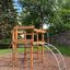 Sherwood wooden playhouse in un parco con alberi e un muro di pietra sullo sfondo.