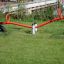 Seesaw rosso su un parco giochi erboso con supporto in gomma nera.