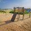 Kampinos wooden playhouse in un parco giochi esterno sabbioso in riva al mare.