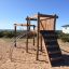 Kampinos wooden playhouse in un'area esterna sabbiosa con elementi di arrampicata e uno scivolo.