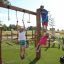 Bambini che giocano sulla struttura del parco giochi Alv con pali di legno, corde per arrampicarsi e arco metallico sotto
