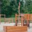 Struttura da esterno in legno con Nature Ship Sandbox in un contesto di parco giochi.