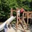 Bambini che giocano su un set da parco giochi in legno Alstad con scivolo e struttura per arrampicarsi.