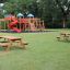 Larchwood Table & Bench in un parco con un'area giochi sullo sfondo.