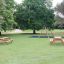 Larchwood Table & Bench in un contesto di parco con alberi e un'area giochi.