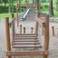 Ponte da parco giochi in legno Dolomiti con rete da arrampicata in un contesto di parco.