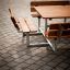 Set da esterno Table & Bench Quadro con sedute in legno e struttura in metallo su superficie pavimentata.