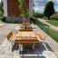 Set da esterno in legno Table & Bench Quadro su un'area pavimentata con vegetazione sullo sfondo