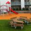 School Table & Bench in un contesto di parco giochi con uno scivolo e una struttura da arrampicata sullo sfondo
