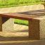 Panchina da parco all'aperto Vega con doghe in legno e supporti in cemento su un camminamento lastricato in mattoni.