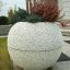 Fioriera da giardino in pietra 'Globe' con piante vivaci davanti a una casa.