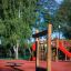 Attrezzature da gioco in legno Barrel su una superficie di sicurezza rossa con alberi e parco giochi sullo sfondo
