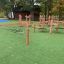Struttura da arrampicata per parco giochi Sahara con pali di legno e corde su erba artificiale.