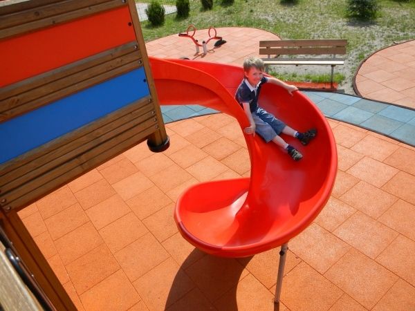 Bambino che gioca su uno scivolo a spirale rosso su Rubber Tiles 90