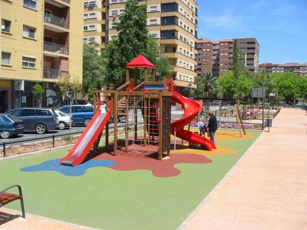 Parco giochi con scivoli rossi e pavimentazione colorata Wetpour 80 in un contesto urbano.