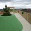 Area giochi su un tetto con superficie di sicurezza verde Wetpour 100 e strutture da gioco in legno.