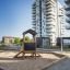 Playhouse Nature all'aperto in un parco giochi sabbioso con alti edifici residenziali sullo sfondo.
