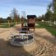 Playhouse Nature in un parco giochi soleggiato con una sabbiera e una giostra