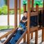 Bambino che gioca su Knight's Castle Nature playhouse with slide.