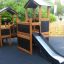 Tower Nature wooden playhouse with slide in un contesto di parco giochi.