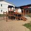 Tower Nature wooden playhouse with slide su un parco giochi sabbioso.