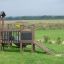 Fortress Nature playhouse with slide su un campo erboso con bambini che giocano