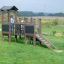 Fortress Nature playhouse with slide in un campo verde con un bambino che gioca.