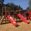 Struttura da parco giochi castello Mastodon con scivolo, con scivoli rossi ed elementi di arrampicata in legno.