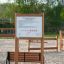 Cartello per parco giochi Rules Tab con norme d'uso montato su struttura in legno in un'area giochi sabbiosa all'aperto