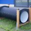 Tunnel da gioco per bambini realizzato in tubo corrugato nero e telai in legno su un'area erbosa.