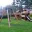 Altalena in legno Swing Frame (single swing) in un parco giochi con struttura per arrampicarsi e scivolo.
