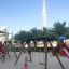Swing Frame (single swing, wide) in un parco giochi soleggiato con bambini che giocano.