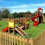 Parco giochi in legno Mini play con scivoli, strutture da arrampicata e altalene in un'area erbosa recintata.