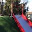 Hill Slide Wide SLW180, scivolo rosso e argento su una collina di erba artificiale in un parco giochi.