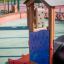 Casetta gioco intelligente in legno con scivolo e pannello alfabetico in un parco giochi.