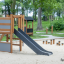 Grocer's single slide in legno naturale e grigio in un parco giochi.