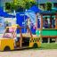 Bambino che gioca in un veicolo da parco giochi giallo Taxi vicino a un trenino verde.