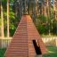 Casetta gioco in legno stile teepee su erba con sfondo di foresta.
