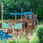Struttura da parco giochi in legno Majestic ship with slide con dettagli blu in un parco verde.