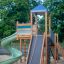Twister castle with slide in un parco giochi con base in sabbia e vegetazione sullo sfondo.